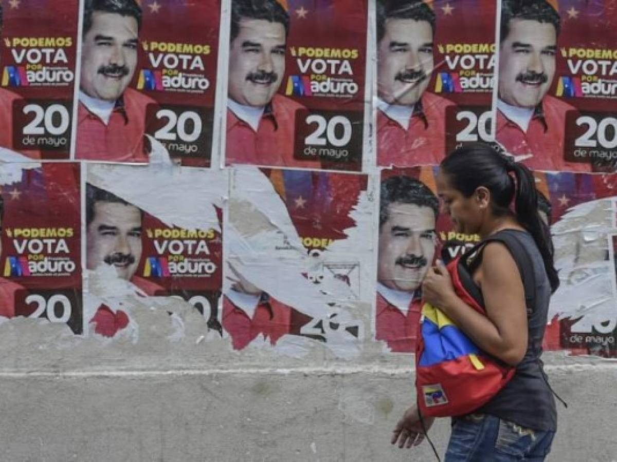 A woman passes by posters of Venezuelan President Nicolas Maduro, in Caracas on May 19, 2018 on the eve of the country's presidential election.Venezuela holds presidential elections on May 20, in which Maduro is seeking a second six-year term. / AFP PHOTO / Juan BARRETO A woman passes by posters of Venezuelan President Nicolas Maduro, in Caracas on May 19, 2018 on the eve of the country's presidential election.Venezuela holds presidential elections on May 20, in which Maduro is seeking a second six-year term. / AFP PHOTO / Juan BARRETO