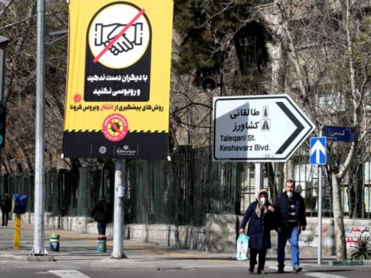 Iranians wearing protective masks walk under a prevention campaign poster for corona virus COVID-19, on March 4, 2020 in the capital Tehran. - Iran has scrambled to halt the rapid spread of the COVID-19 virus, shutting schools and universities, suspending major cultural and sporting events, and cutting back on work hours. (Photo by ATTA KENARE / AFP)