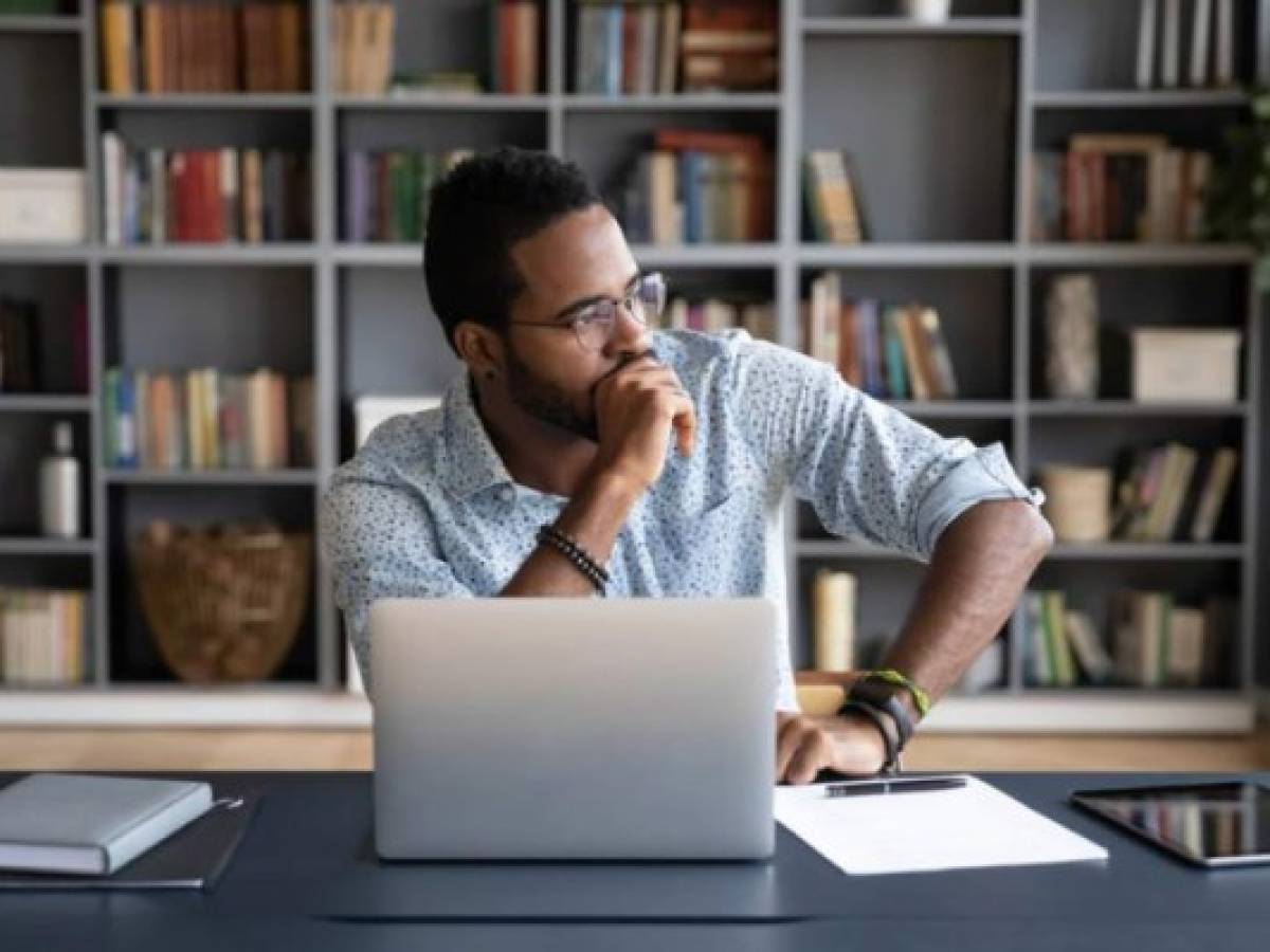 Thoughtful doubtful African businessman in tension sitting at workplace desk near laptop distracted from work makes difficult decision looking at window feels uncertain thinking over problem solution