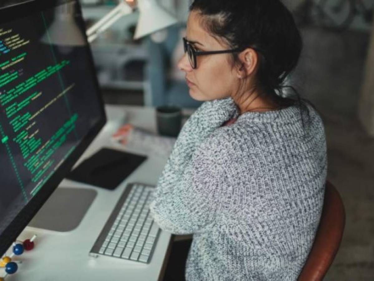 Photo of a young woman sitting at her desktop computer, doing computer programming in her home office
