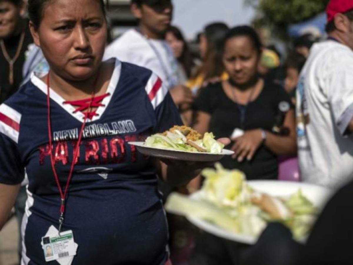 Central American migrants travelling to the United States, receive a plate of paella, cooked by a group of chefs during the 'Paella sin Frontera', (paella without borders) event at El Barretal temporary shelter in Tijuana, Baja California state, Mexico on December 23, 2018. - Chefs from Mexico, Spain and the US took part in the initiative, in solidarity with Central American migrants. (Photo by Guillermo Arias / AFP)