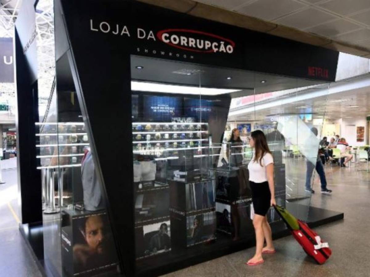 A passenger stops to take a look at the 'Corruption Shop', a kiosk at Brasilia's Airport set up to promote the new Netflix series 'The Mechanism' (O Mecanismo), based on Brazil's mammoth 'Car Wash' graft scandal, on March 28, 2018. The kiosk which is part of an advertising campaign to promote 'O Mecanismo', a Brazilian drama series based on 'Lava Jato' (Car Wash), the largest anti-corruption investigation in Brazil's history, that involves private and state-owned oil and construction companies -on air since March 23, 2018- displays items which supposedly facilitate the life of corrupt persons. / AFP PHOTO / EVARISTO SA