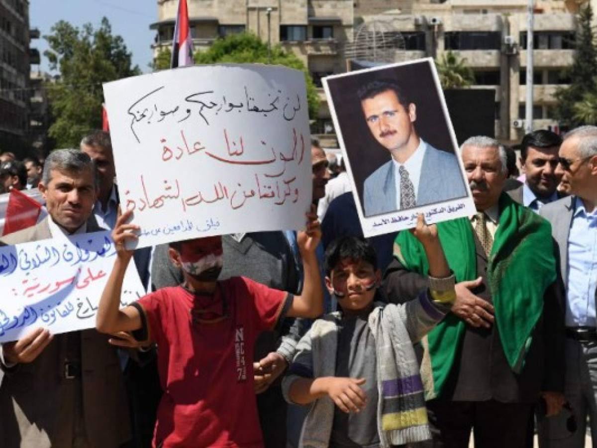 Syrians wave the national flag and wave portraits of President Bashar al-Assad as they gather in Aleppo's Saadallah al-Jabiri square on April 14, 2018, to condemn the strikes carried out by the United States, Britain and France against the Syrian regime. / AFP PHOTO / George OURFALIAN Syrians wave the national flag and wave portraits of President Bashar al-Assad as they gather in Aleppo's Saadallah al-Jabiri square on April 14, 2018, to condemn the strikes carried out by the United States, Britain and France against the Syrian regime. / AFP PHOTO / George OURFALIAN