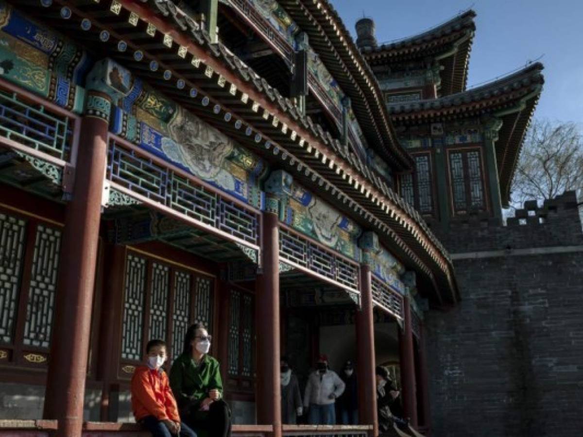 Una madre y su hijo se dejan ver con mascarillas en medio de la preocupación por la propagación del nuevo coronavirus COVID-19, disfrutan de la luz del sol mientras se sientan en un parque en Beijing el 14 de marzo de 2020. Foto NICOLAS ASFOURI / AFP)