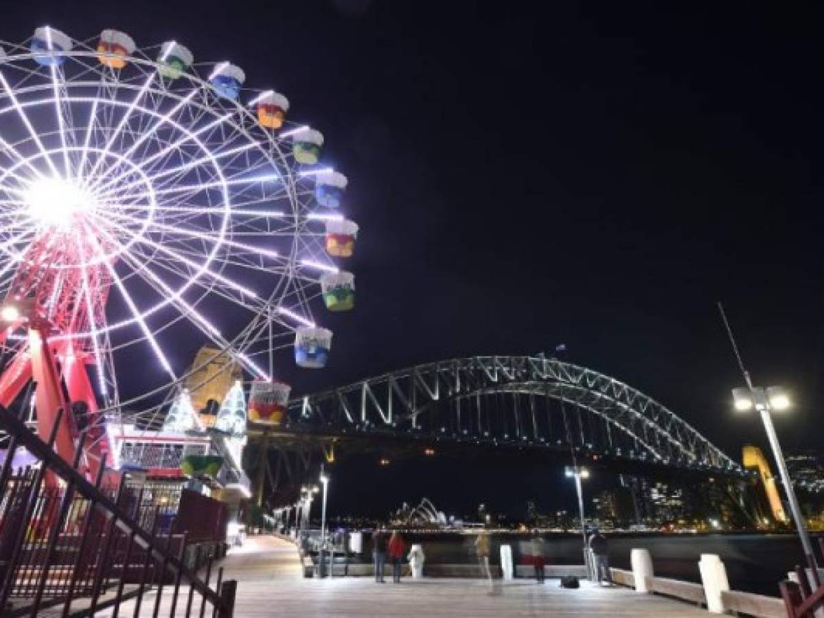 The Sydney Harbour Bridge, the Opera House and the ferris wheel are seen before being plunged into darkness from Sydney's Luna Park for the Earth Hour environmental campaign on March 30, 2019. - The lights went out on two of Sydney's most famous landmarks for the 12th anniversary of the climate change awareness campaign Earth Hour, among the first landmarks around the world to dim their lights for the event. (Photo by PETER PARKS / AFP)