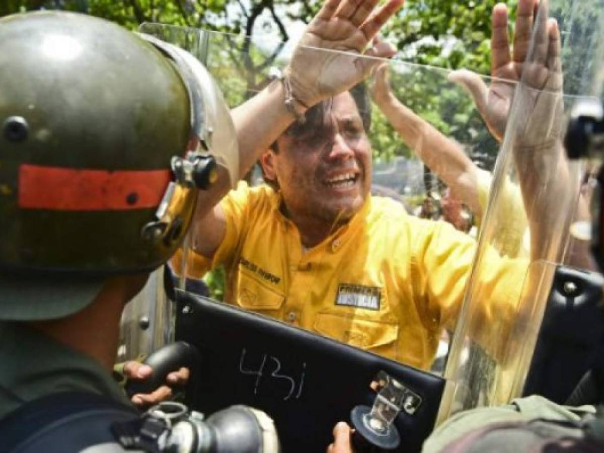 Venezuelan opposition Deputy Carlos Paparoni pushes the shields of riot policemen during a march in Caracas on April 26, 2017. Protesters in Venezuela plan a high-risk march against President Maduro Wednesday, sparking fears of fresh violence after demonstrations that have left 26 dead in the crisis-wracked country. / AFP PHOTO / RONALDO SCHEMIDT