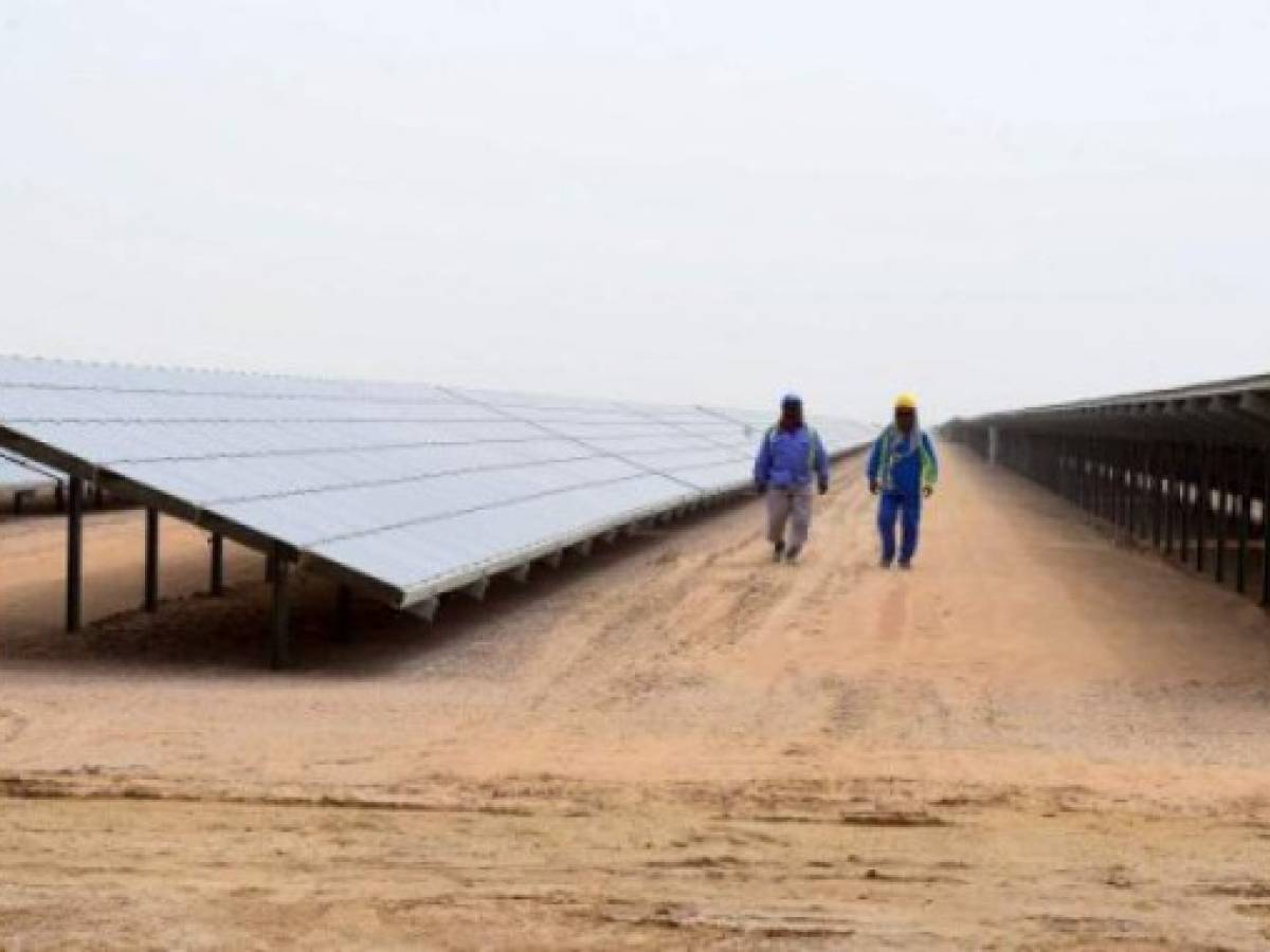 Employees walk past solar panels at the Mohammed bin Rashid Al-Maktoum Solar Park on March 20, 2017, in Dubai.Dubai completed a solar plant big enough to power 50,000 homes as part of a plan to generate three-quarters of its energy from renewables by 2050. / AFP PHOTO / STRINGER