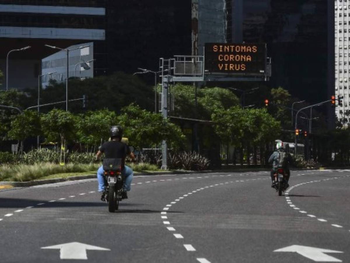 Two bikers ride in front of an electronic traffic board displaying a message on the Dos ciclistas viajan frente a un tablero de tráfico electrónico que muestra un mensaje sobre los síntomas del coronavirus en la avenida Libertador, en Buenos Aires, el 13 de marzo de 2020. Foto RONALDO SCHEMIDT / AFP.