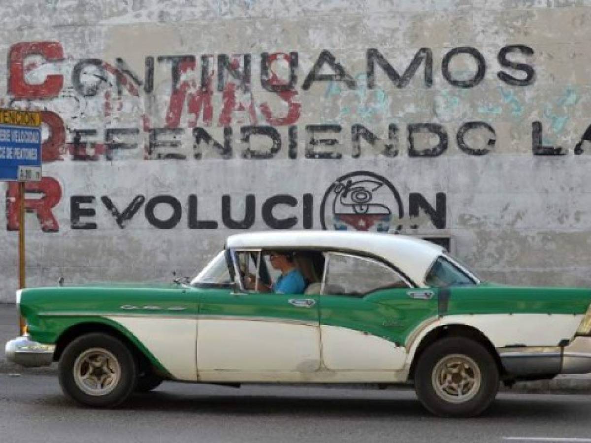 A car drives past a wall reading 'We Continue Defending Revolution' referring to Committees for the Defense of the Revolution (CDR), in Havana on March 20, 2018.The CDR, which were created by Cuban late leader Fidel Castro in 1960 as surveillance and unconditionality symbols, will remain as community spaces after Raul Castro leaves Cuba's presidency. / AFP PHOTO / Yamil LAGE / TO GO WITH AFP STORY BY MOISES AVILA AND CARLOS BATISTA