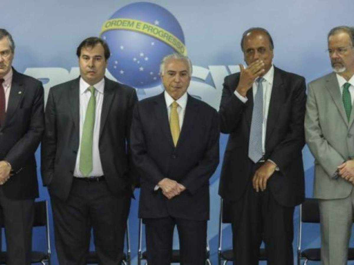 (L to R) Brazilian Justice Minister Torquato Jardim, Brazilian President Michel Temer, deputy Rodrigo Maia, Rio de Janeiro's Governor Luiz Fernando Pezao and Defense Minister Raul Jungmann are pictured during the signature of a decree to send in the army to lead public safety in Rio de Janeiro state, at the Planalto Palace in Brasilia, on February 16, 2018.Army patrols are already used in Rio's favelas ruled by drug gangs, but the decree will now give the military full control of security operations in Rio state, which the president said had virtually been seized by organized crime gangs. / AFP PHOTO / Sergio LIMA
