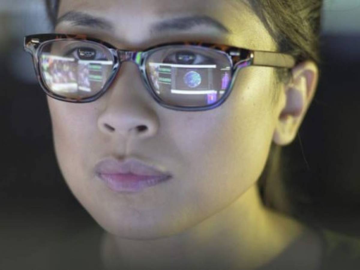 Close up stock image of a young asian woman staring at a computer screen which is reflected in her glasses. The reflection depicts graphs; people & data.