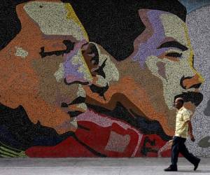 A man walks past a mosaic depicting late Venezuelan President Hugo Chavez (L) and Venezuelan president Nicolas Maduro on a wall in Caracas on January 30, 2019. - Venezuelan President Nicolas Maduro said he is willing to negotiate with the opposition and hold early congressional elections, in a concession as opponents plan another big demonstration. (Photo by Juan BARRETO / AFP)