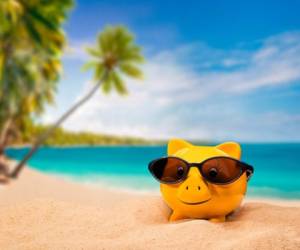 Gelbes Sparschwein mit Sonnenbrille mit einem tropischen Strand im Hintergrund