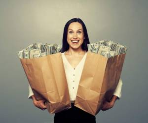 excited businesswoman holding two paper bags with money and smiling. photo in studio over grey background