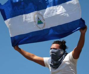 An opposition protester displays a Nicaraguan flag from a shopping mall where he and others took refuge after they were prevented by the Nicaraguan riot police from demonstrating against the government to demand the release of those arrested for taking part in anti-government protests, in the surroundings of the Centroamerica roundabout in Managua on March 16, 2019. - Nicaragua on Friday released 50 prisoners held for participating in anti-government protests, giving a fresh impetus to peace talks on ending the country's long running political crisis. More than 700 people were detained during a deadly crackdown on rallies that began last April and quickly grew into broad opposition to President Daniel Ortega iron-fisted rule. (Photo by Maynor VALENZUELA / AFP)