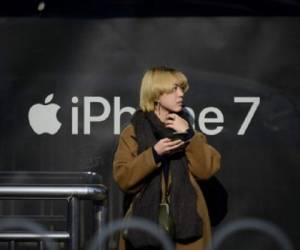 A woman looks on as she stands in front of a billboard promoting Apple's iPhone 7 at a bus stop in Beijing on November 24, 2016. China will be handed the opportunity to reshape the rules for global trade and profit from a more isolated US if President-elect Donald Trump carries out his pledge to abandon the landmark TPP pact, observers say. / AFP PHOTO / WANG ZHAO