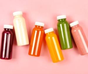 Bottles of multicolored smoothies or juices on pink background. Flat lay style.