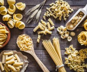 Top view of a rustic wooden table filled with a large Italian pasta variety. The types of pasta included are spaghetti, orecchiette, conchiglie, rigatoni, fusilli, penne and tagliatelle. Predominant colors are yellow and brown. DSRL studio photo taken with Canon EOS 5D Mk II and Canon EF 100mm f/2.8L Macro IS USM