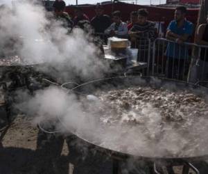 Central American migrants travelling to the United States, look on as chefs cook a paella, during the 'Paella sin Frontera', (paella without borders) event at El Barretal temporary shelter in Tijuana, Baja California state, Mexico on December 23, 2018. - Chefs from Mexico, Spain and the US took part in the initiative, in solidarity with Central American migrants. (Photo by Guillermo Arias / AFP)