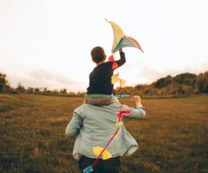 Little boy is running a kite with his father, on a beautiful day they are spending outdoors in nature
