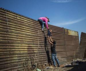 -- AFP PICTURES OF THE YEAR 2018 --A group of Central American migrants climb the border fence between Mexico and the United States, near El Chaparral border crossing, in Tijuana, Baja California State, Mexico, on November 25, 2018. - Hundreds of migrants attempted to storm a border fence separating Mexico from the US on Sunday amid mounting fears they will be kept in Mexico while their applications for a asylum are processed. An AFP photographer said the migrants broke away from a peaceful march at a border bridge and tried to climb over a metal border barrier in the attempt to enter the United States. (Photo by Pedro PARDO / AFP)