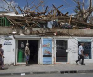 People walk by a damaged building in which a shop has re-opened on September 15, 2017 in Marigot on the French Caribbean island of Saint Martin after the island was hit by Hurricane Irma.The Category 4 hurricane, which struck in 1995, killed 19 people in St Martin, Antigua, Barbuda, St Barts and Anguilla and left tens of thousands homeless. Irma left 15 dead on both sides of St Martin. / AFP PHOTO / Helene Valenzuela