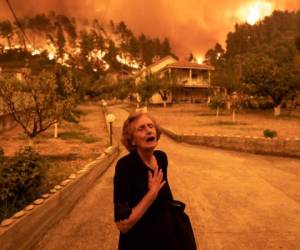 An elderly resident reacts as a wildfire approaches her house in the village of Gouves, on the island of Evia, Greece, on Sunday, Aug. 8, 2021. Thousands of residents were evacuated from the Greek island of Evia by boat after wildfires hit Greeces second biggest island. Photographer: Konstantinos Tsakalidis/Bloomberg via Getty Images