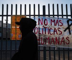 <i>Un migrante pasa por un letrero que dice “No más políticas inhumanas” después de pasar la noche afuera del centro de detención migratoria donde 38 migrantes murieron durante un incendio en Ciudad Juárez, estado de Chihuahua, México el 29 de marzo de 2023. (Foto de Guillermo Arias / AFP)</i>