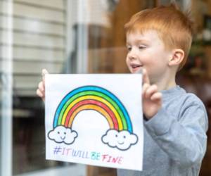 Young Boy sticking his drawing on home window during the Coronavirus Covid-19 crisis, view from outside the house. Many people are putting a rainbow to tell neighbours that people inside this house are ok. #Stayathome #itwillbefine #cavabienaller