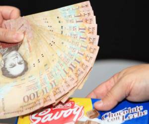 San Cristobal, Venezuela - July 23, 2016: Lady pays with 18 bills of 100 bolivares to buy a local bar chocolate today in a convenience store in San Cristobal, Venezuela. The one-hundred bill is the highest face value of the Venezuelan currency that according to today's rate in the black market, the reference price for the great mayority of products and services in the country, is about one dollar. That little value of the currency along with an inflation rate for 2016 estimated around 700% and a contraction of the economy with a forecast of about -10% GDP for the year, both figures just released by the IMF, shows the deep economic problems that the Latin American oil producer country has at the moment. Average workers are gong through hard times when this chocolate bar at Bs. 1.800 represents 12% of the minimun legal wage.