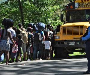 African and Haitian migrants board a bus after going through a 'blind crossing' from Nicaragua to Honduras on their way to the US, as police officers stand guard in Guasaule, Honduras on November 16, 2019. - Uncontrolable migratory flows make it difficult for Honduras to fulfill with the Safe Third Country agreement the country, El Salvador and Guatemala signed with the US, which requires migrants who seek assylum in the US, to apply in those countries first. (Photo by ORLANDO SIERRA / AFP)