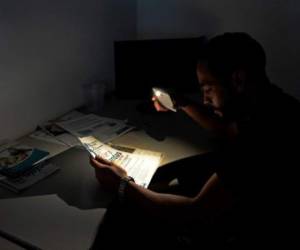 Un hombre utiliza la luz de su móvil como linterna para leer en un apagón que inició el jueves en San Cristobal, Tachira. AFP PHOTO / GEORGE CASTELLANOS