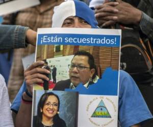 Un nicaragüense sostiene un cartel con los retratos de Miguel Mora y Lucía Pineda, periodistas detenidos por el régimen de Daniel Ortega. Mora fue acusado de conspiración y terrorismo, mientras que su canal 100% Noticias fue sacado del aire. Foto AFP