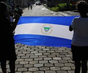 Two woman display a Nicaraguan national flag during the funeral procession of Bismark Martinez, who died in hospital three months after being injured during anti-government protests, as they take his coffin to the cemetery in Masaya, Nicaragua, on September 17, 2018. - Thousands of demonstrators marched Sunday through Nicaragua's capital Managua to demand the resignation of President Daniel Ortega and the liberation of hundreds detained during months of deadly government repression that have left more than 300 people dead. (Photo by Inti OCON / AFP)