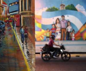 <i>Un motociclista pasa junto a un mural en una avenida central de Tegucigalpa el 8 de febrero de 2024. La capital hondureña se ha convertido en una galería al aire libre, donde artistas locales dan color y vida a este antiguo pueblo minero.</i>