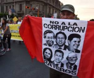 Un peruano sostiene una bandera del Perú con los rostros de Alberto Fujimori, Alejandro Toledo, Ollanta Humala, Alan Garcia, además de la exprimera dama Nadine Heredia sobre quienes pesan señalamientos de corrupción.
