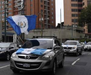People flutter Guatemalan flags from their cars during a motorcade to protest demanding Guatemalan President Alejandro Giammattei to end confinement measures imposed since March against the spread of the new coronavirus and prevent a possible collapse of the economy, in Guatemala City on June 18, 2020. - (Photo by Johan ORDONEZ / AFP)