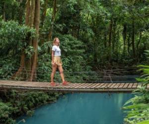 Young woman wandering in tropical rainforest walking on bridge over turquoise lagoon, Costa Rica
