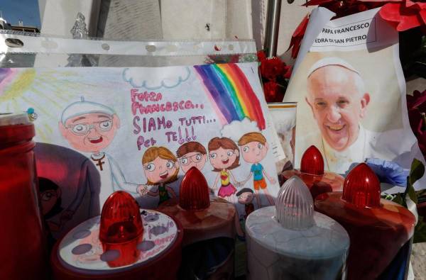 <i>Un dibujo y una fotografía del papa Francisco bajo la estatua de Juan Pablo II, frente al Hospital Agostino Gemelli, donde se encuentra hospitalizado desde el 14 de febrero debido a una infección en las vías respiratorias. EFE/EPA/GIUSEPPE LAMI</i>