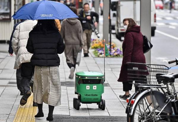 <i>Los peatones caminan junto a un robot no tripulado (C) mientras navega por una calle durante una demostración de un servicio de entrega de robots realizado por Uber Eats Japan, Mitsubishi Electric y el desarrollador de robots Cartken en el centro de Tokio el 5 de marzo de 2024. FOTO Richard A. Brooks/AFP</i>