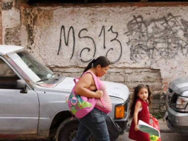 residentes pasan por un grafitti hecho por la Mara Salvatrucha (MS-13) en el barrio El Bosque, Tegucigalpa, en mayo, 2017. AFP PHOTO / ORLANDO SIERRA / TO GO WITH AFP STORY BY NOE LEIVA