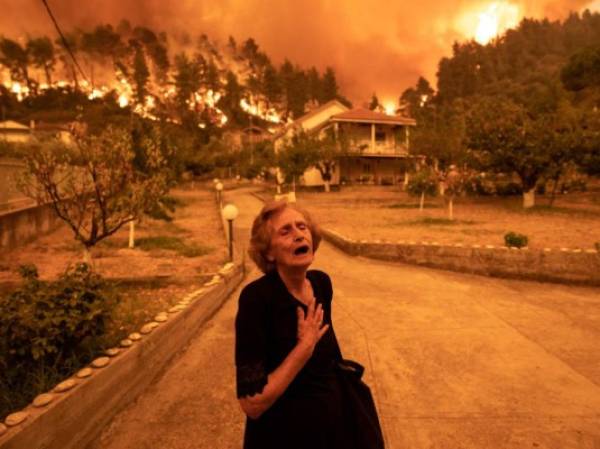 An elderly resident reacts as a wildfire approaches her house in the village of Gouves, on the island of Evia, Greece, on Sunday, Aug. 8, 2021. Thousands of residents were evacuated from the Greek island of Evia by boat after wildfires hit Greeces second biggest island. Photographer: Konstantinos Tsakalidis/Bloomberg via Getty Images