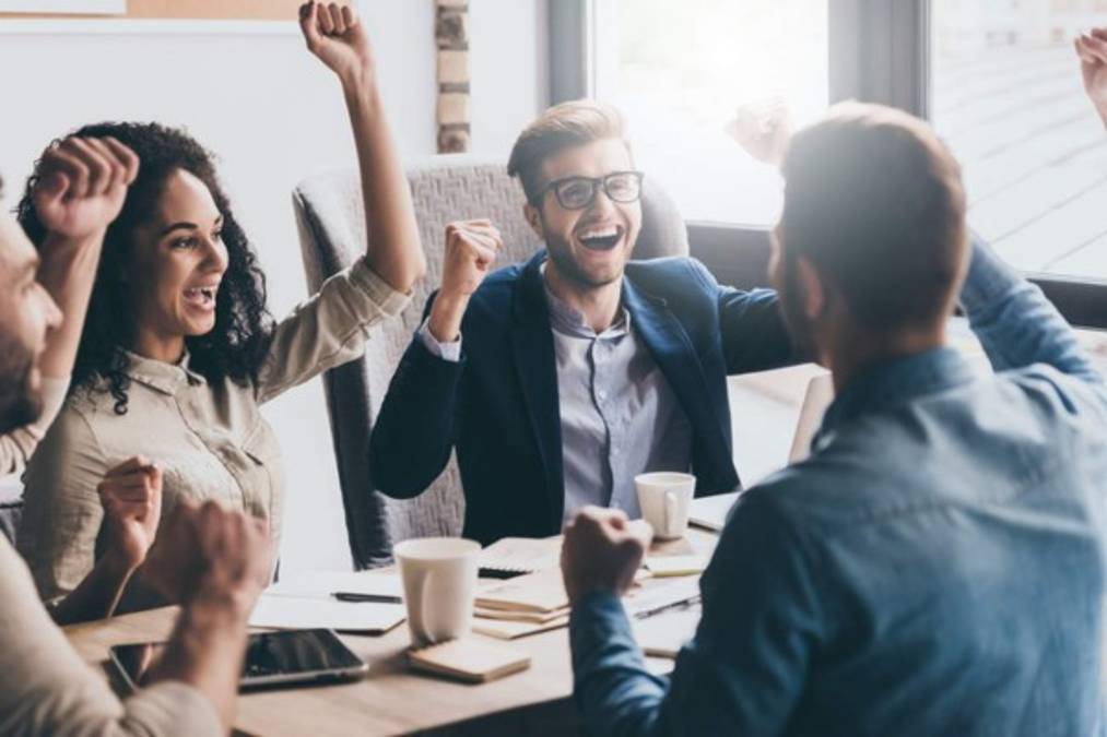 Cheerful young people looking excited while sitting at the office table at the business meeting
