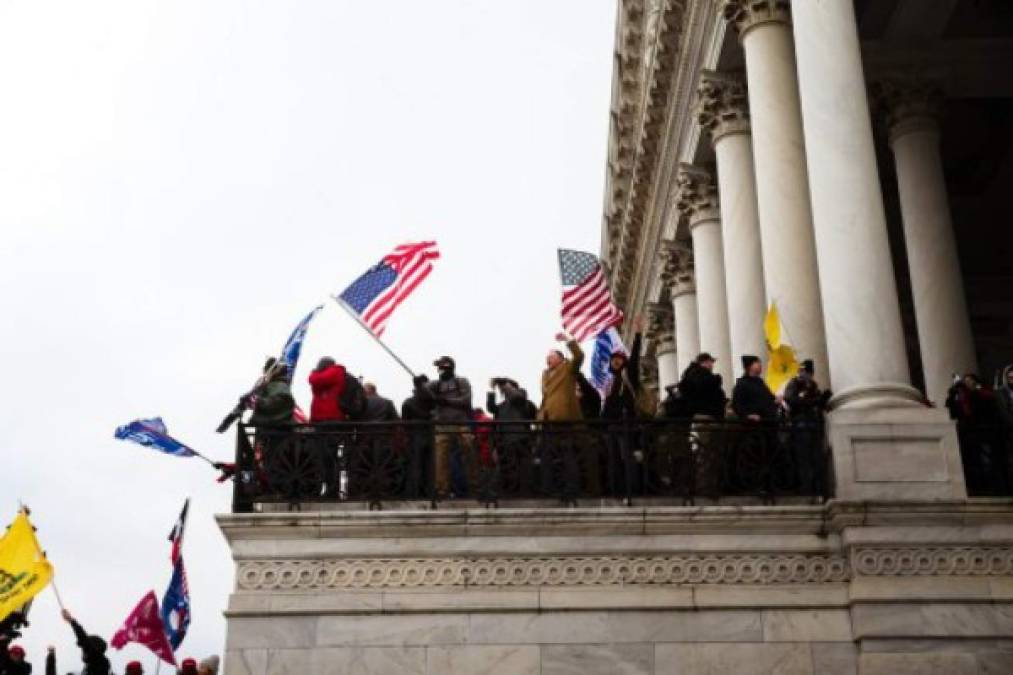 Simpatizantes del presidente Trump ondean banderas en el Capitolio. Las protestas interrumpieron el conteo de los votos del Colegio Electoral que realizaba el Congreso para formalizar la victoria del presidente electo de EEUU, Joe Biden.<br/> Jon Cherry/Getty Images/AFP