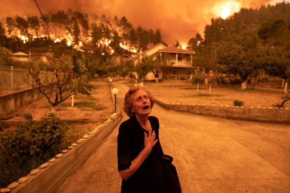 An elderly resident reacts as a wildfire approaches her house in the village of Gouves, on the island of Evia, Greece, on Sunday, Aug. 8, 2021. Thousands of residents were evacuated from the Greek island of Evia by boat after wildfires hit Greeces second biggest island. Photographer: Konstantinos Tsakalidis/Bloomberg via Getty Images