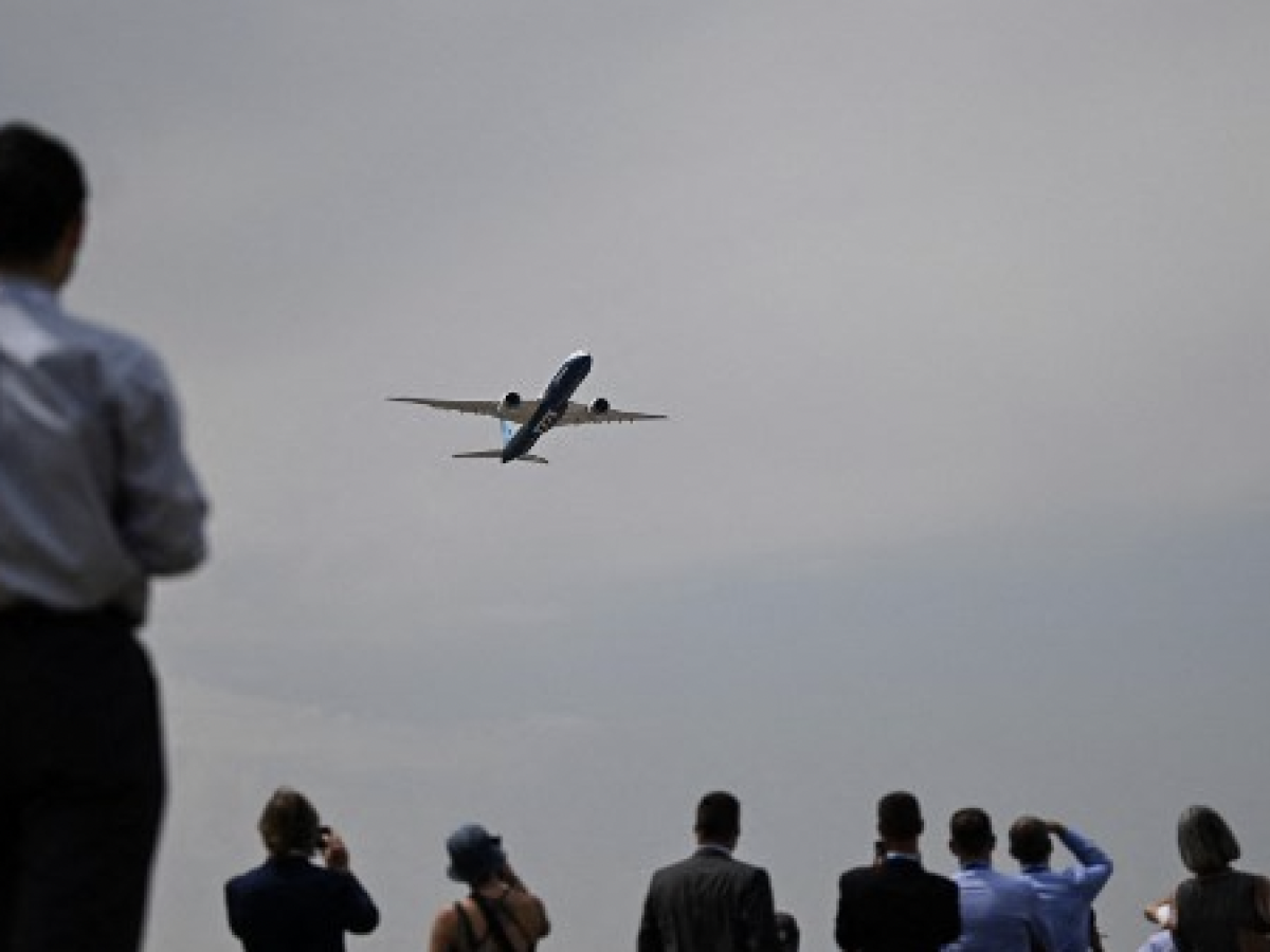 Los visitantes miran un avión Boeing 777X que sobrevuela durante la exhibición aérea del Salón Aeronáutico de Farnborough el 18 de julio de 2022.