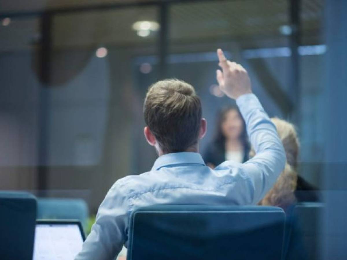 A group of businesspeople having a meeting and one businessman raising his hand with a question during the presentation