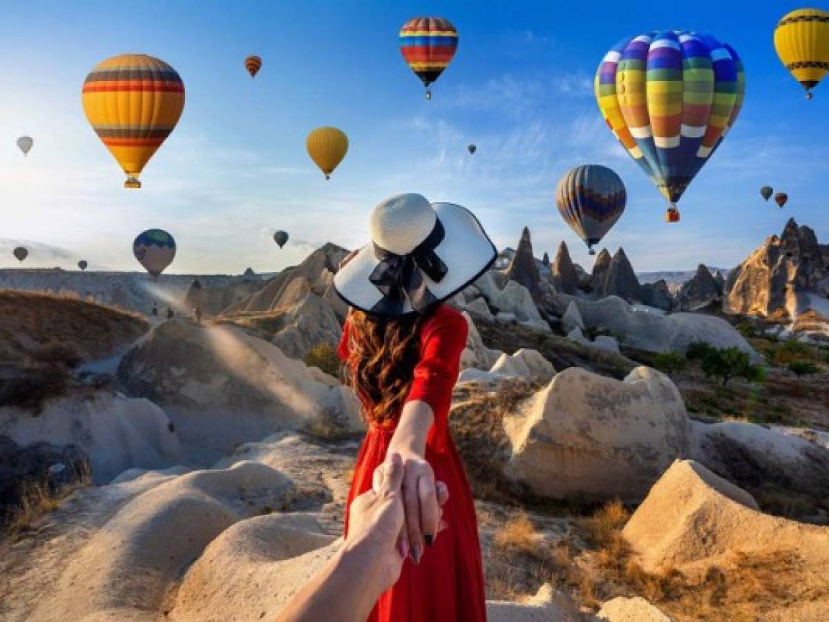 Turista sosteniendo la mano de un hombre, llevándolo a hacia los globos aerostáticos en Capadocia, Turquía.
