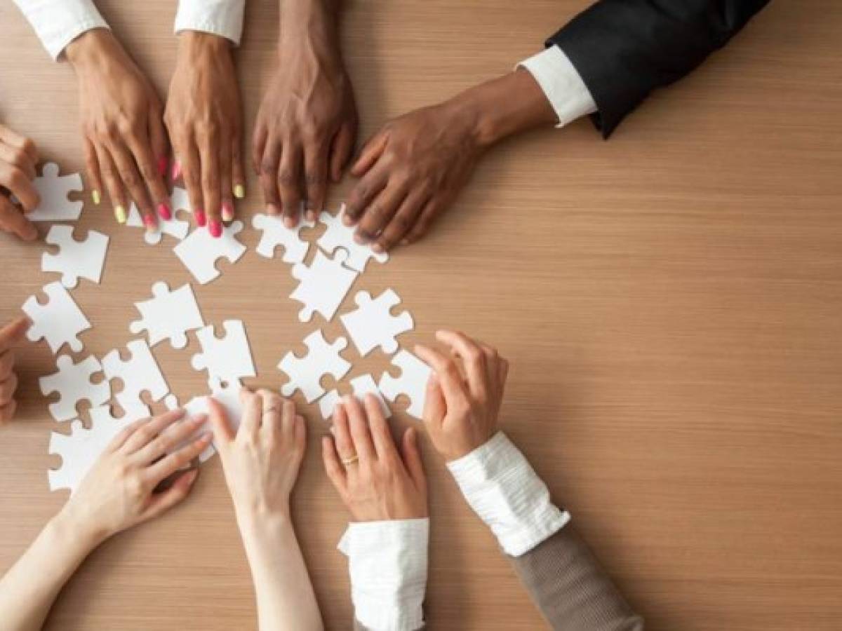 Hands of multi-ethnic team assembling jigsaw puzzle, multiracial group of black and white people joining pieces at desk, successful teamwork concept, help and support in business, close up top view