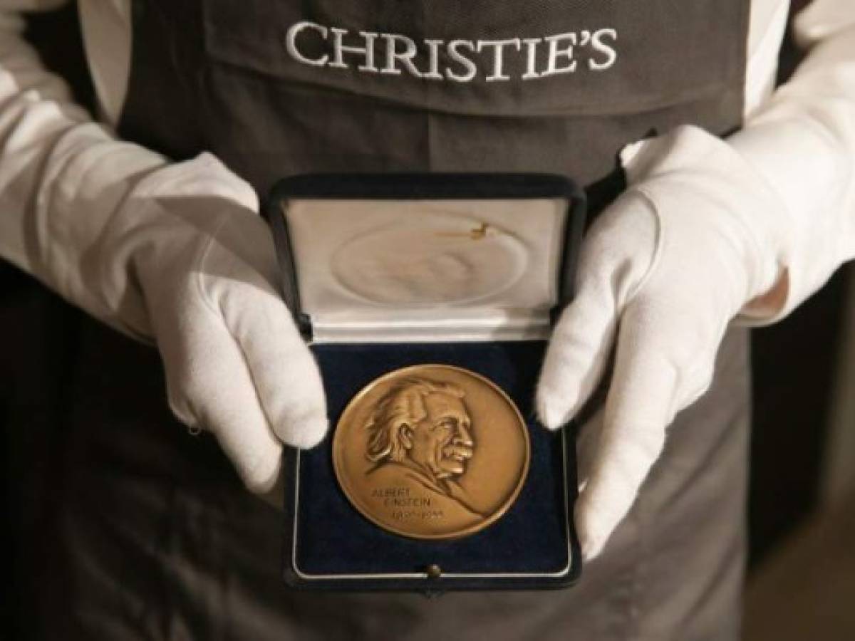 A gallery employee holds an Albert Einstein Medal awarded to late British theoretical physicist Stephen Hawking during a photocall for the sale of personal items from Hawking's estate at Christie's auction house in London on October 30, 2018. (Photo by Daniel LEAL-OLIVAS / AFP)